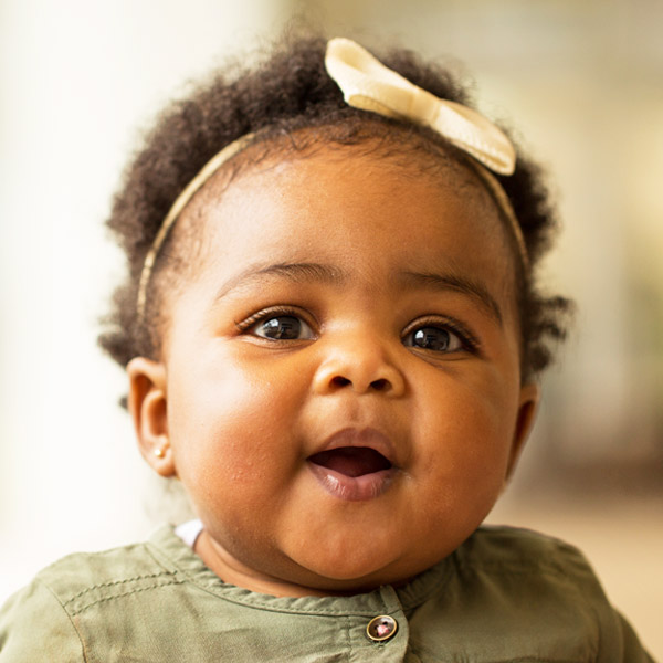 A joyful baby with a bow headband smiles brightly.