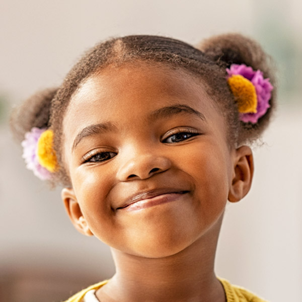 A happy girl grins confidently, her hair adorned with colorful accessories, radiating joy.