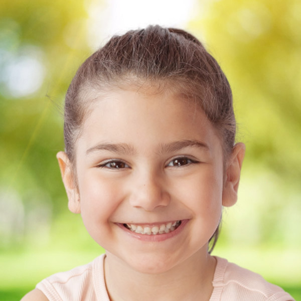 A smiling girl with a bright expression enjoys the outdoors, radiating joy and innocence.