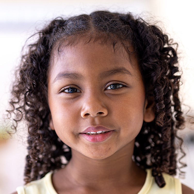 A confident girl with curly hair smiles softly, capturing a moment of warmth and happiness.