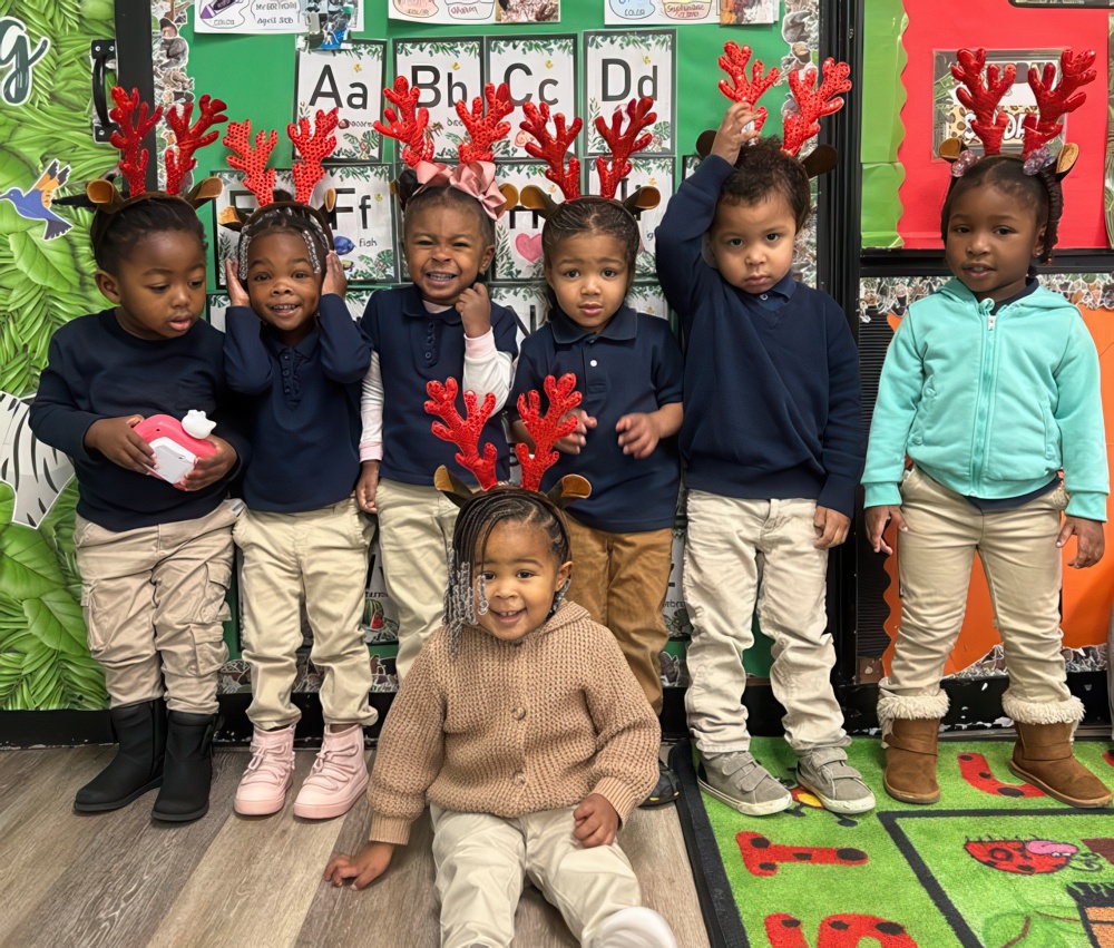 Children wear festive antler headbands and smile together in a playful classroom setting, celebrating the holiday.