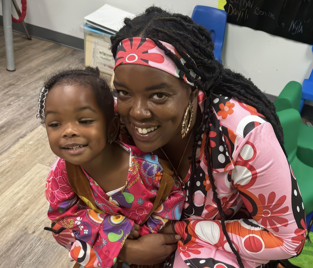 A smiling mother and child wear matching colorful outfits, posing together happily in a cheerful setting.