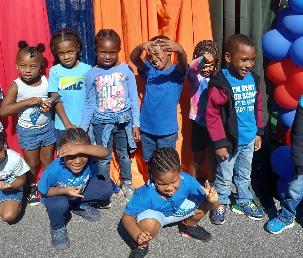 A group of kids in blue outfits poses playfully, smiling and making fun gestures against a vibrant backdrop.