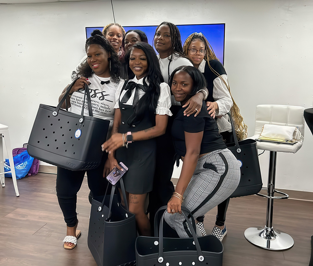 A group of teacher poses cheerfully with stylish bags, showcasing camaraderie in a modern indoor setting.