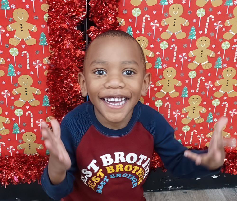 A cheerful child smiles widely, excitedly gesturing in front of a festive backdrop decorated with gingerbread men.