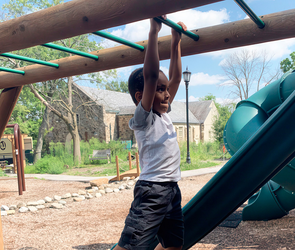 A boy hangs from a playground structure, focused and determined, enjoying a fun day outdoors.