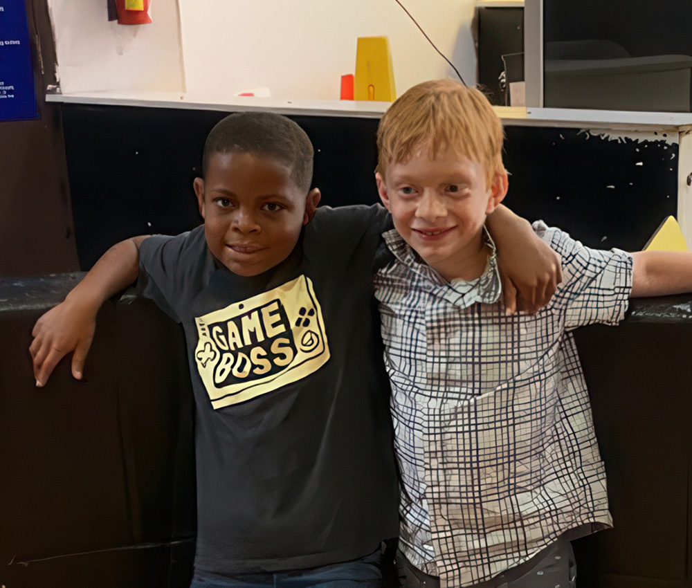 Two boys smile and pose together, one wearing a "Game Boss" shirt, showcasing friendship and camaraderie.