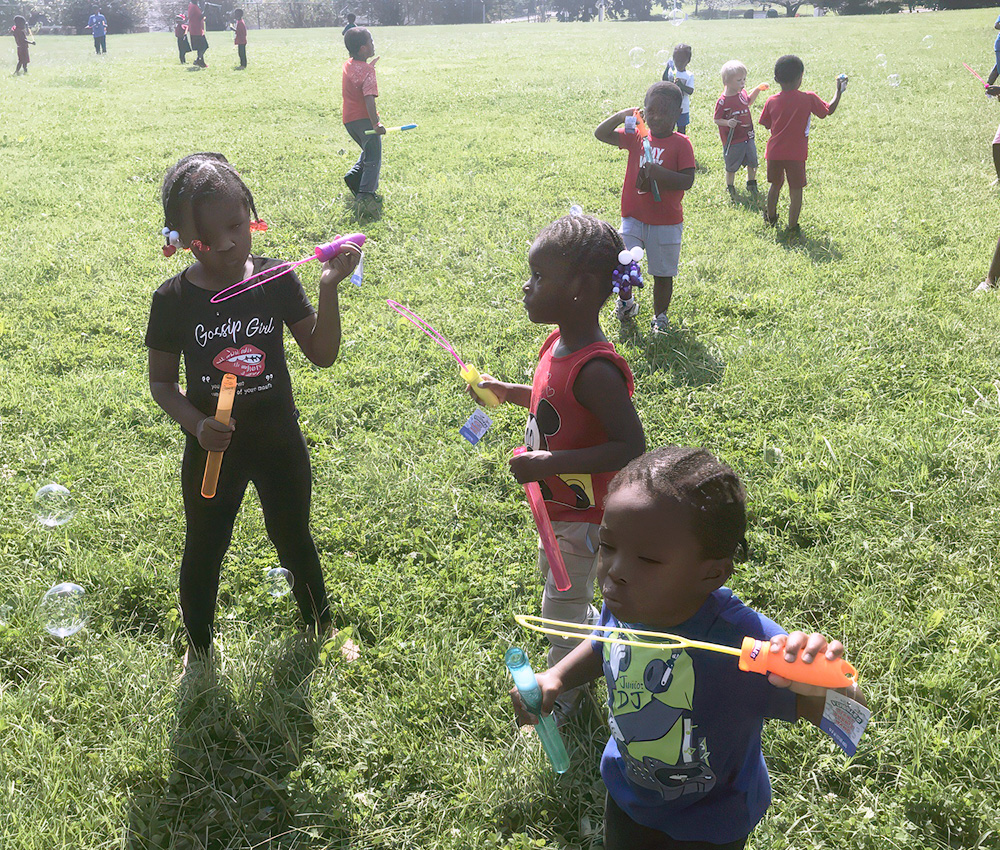 Children play with bubble wands in a grassy field, joyfully creating bubbles and enjoying a sunny day outdoors.