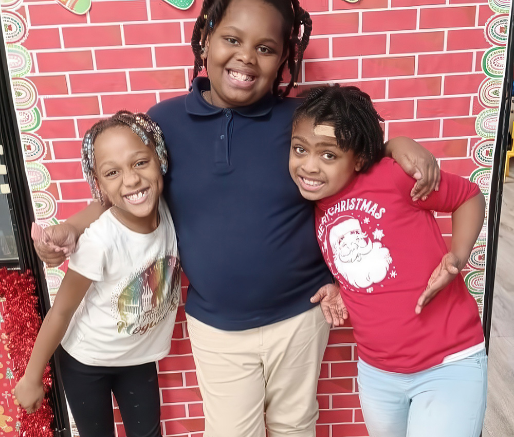 Three girls pose together with big smiles in front of a festive backdrop, radiating joy and friendship.