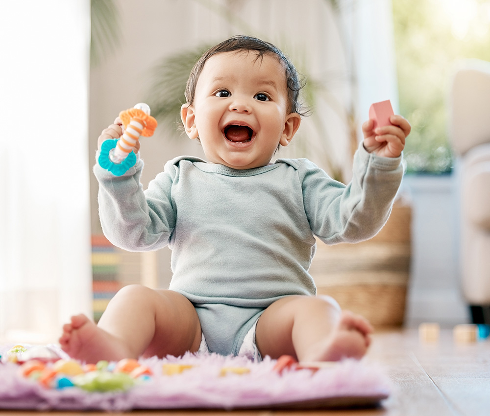 A cheerful baby sits on a soft mat, holding colorful toys and laughing joyfully, surrounded by a warm, inviting space.