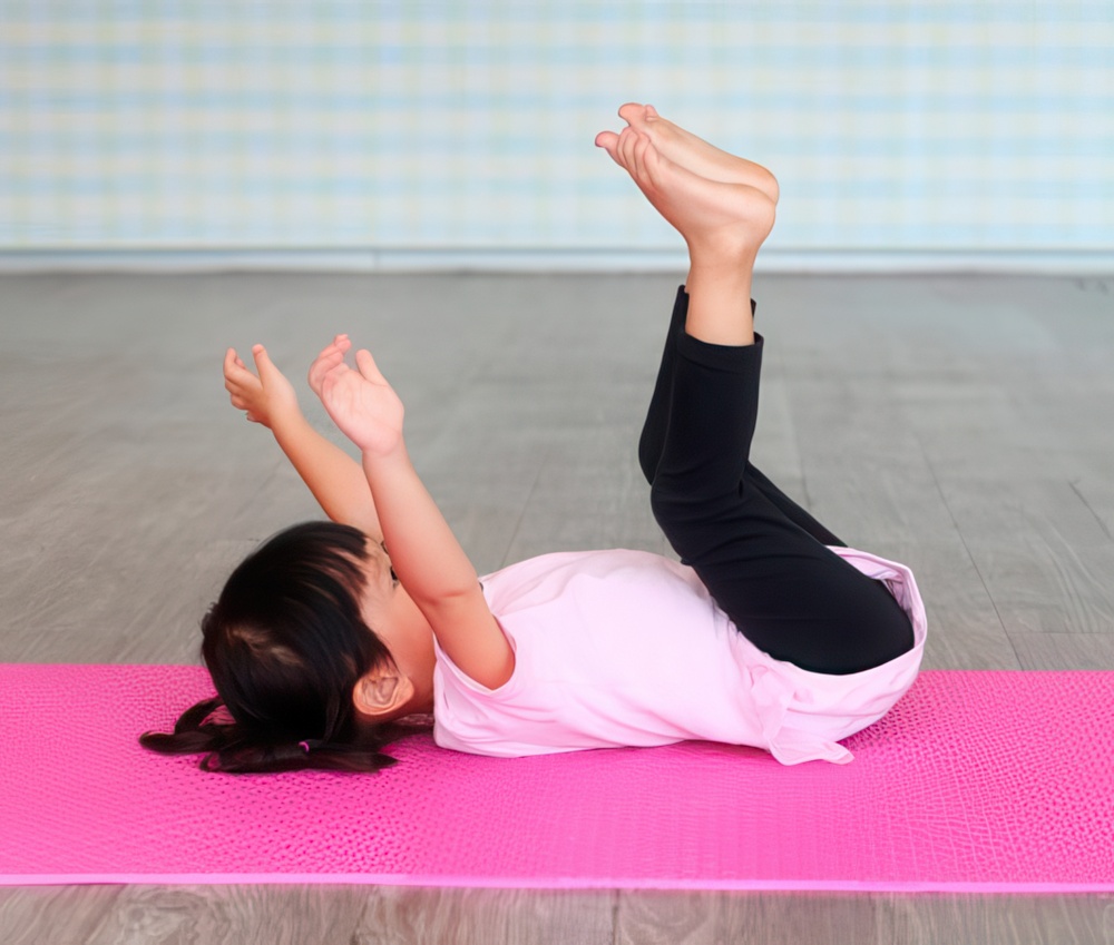 A young child lies on a pink yoga mat, playfully raising their legs and arms in the air, enjoying a fun moment.