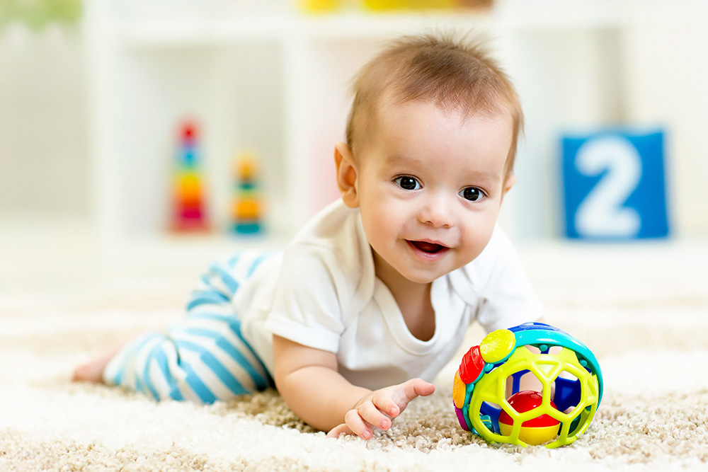 A happy baby crawls on a soft rug, reaching for a colorful toy ball, showcasing curiosity and joy in playtime.