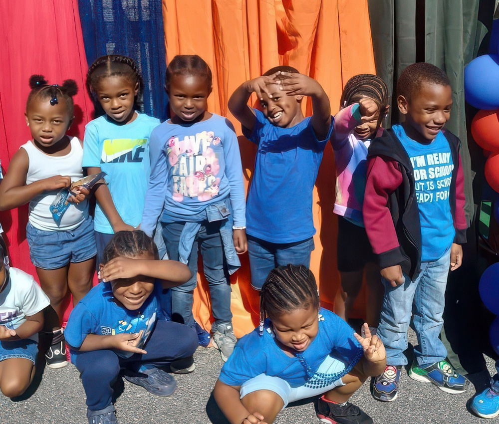 A group of cheerful children poses in blue outfits, making playful gestures in front of a colorful backdrop.