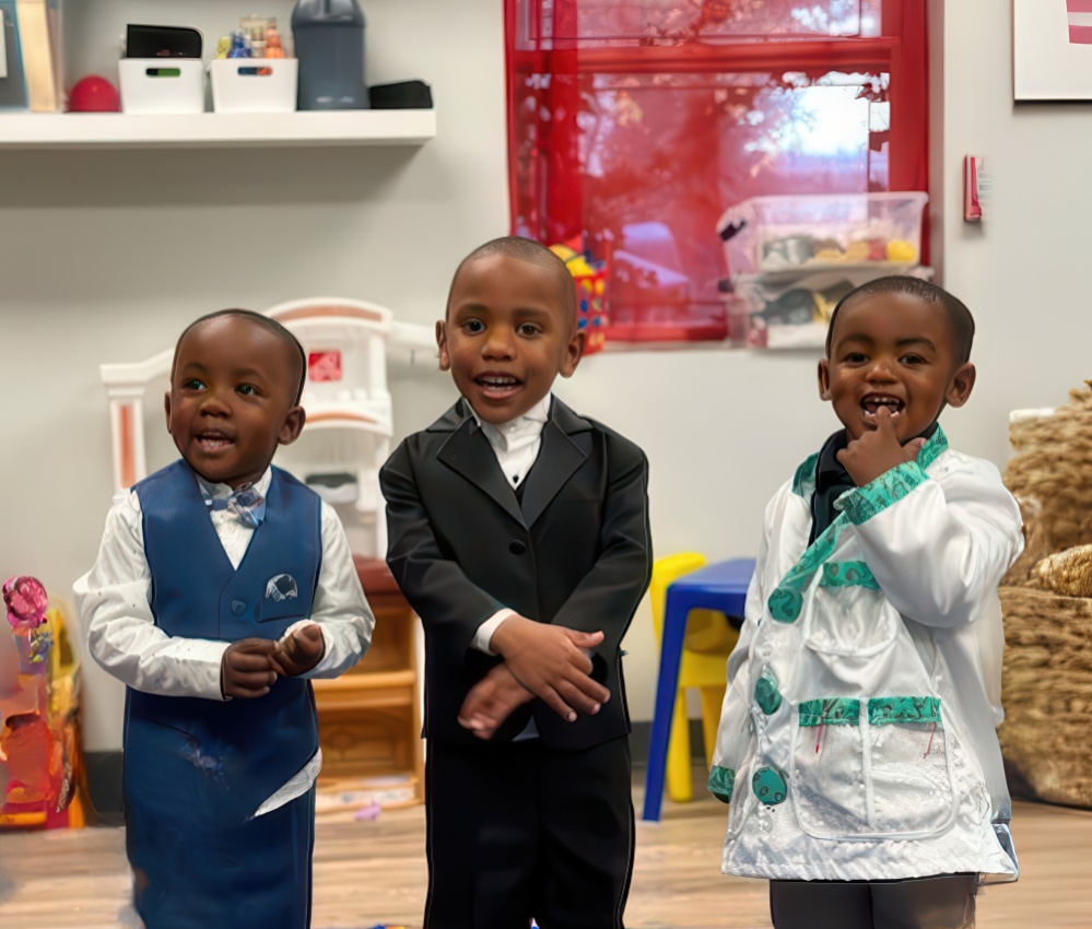 Three young children dressed in formal outfits smile and pose together, showcasing their stylish attire in playful setting.