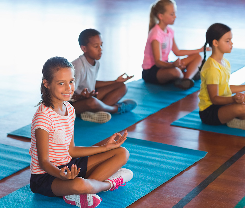 Children practice mindfulness on mats, with a girl smiling as she meditates, creating a calm and focused atmosphere.