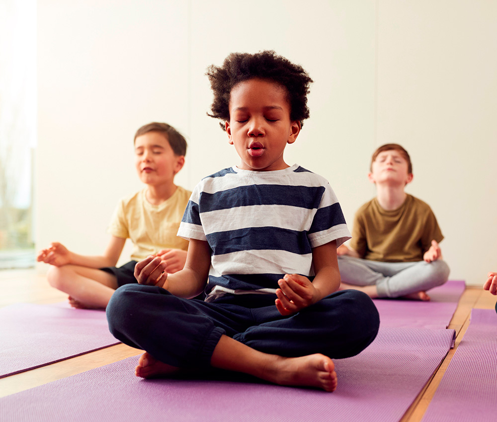 Three boys practice meditation on yoga mats, eyes closed, focusing on their breath in a calm setting.